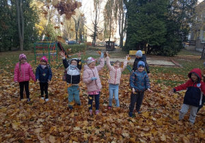 Dzieci śmieją się i podrzucają liście do góry.