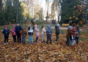 Dzieci śmieją się i podrzucają liście do góry.