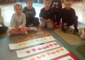 dzieci siedzą na dywanie przy kolorowych listkach