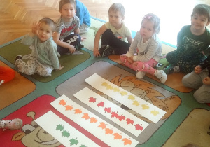 dzieci siedzą na dywanie przy kolorowych listkach