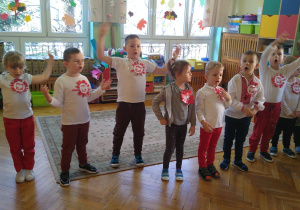 Dzieci ubrane w stroje w kolorach białym i czerwonym śpiewają piosenkę