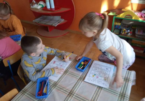 Dzieci wykonują karty pracy przy stoliku