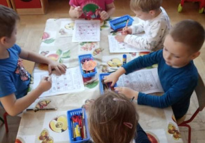 Dzieci wykonują karty pracy przy stoliku