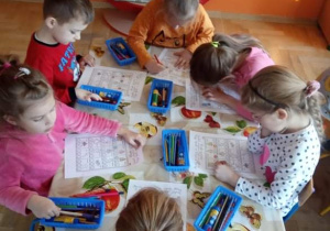 Dzieci wykonują karty pracy przy stoliku