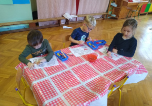Dzieci wykonują karty pracy przy stoliku
