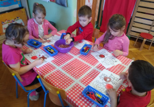 Dzieci wykonują karty pracy przy stoliku
