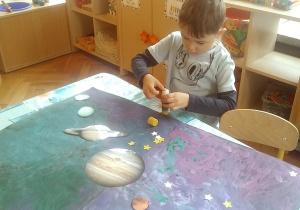 dzieci doklejają gwiazdki i planety na namalowany karton