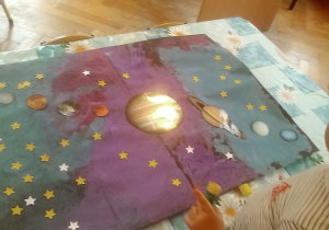 dzieci doklejają gwiazdki i planety na namalowany karton