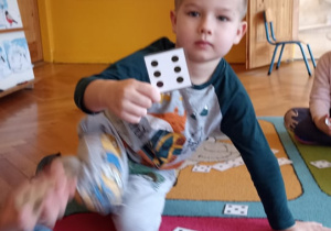 dzieci siedzą na dywanie. na dywwanie leżą karteczki z cyframi