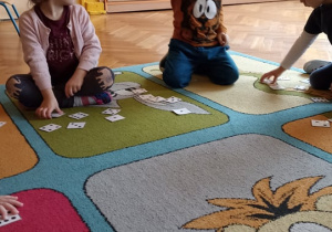 dzieci siedzą na dywanie. na dywwanie leżą karteczki z cyframi