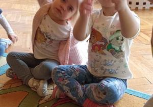 dzieci siedzą na dywanie. na dywwanie leżą karteczki z cyframi