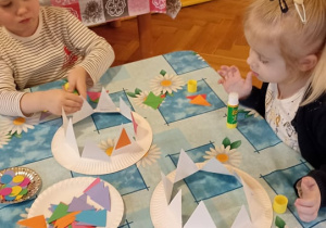 dzieci prezentują czpki karnawałowe wykonane z talerzyków papierowych