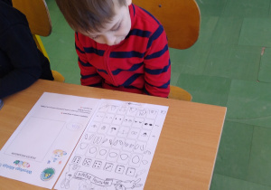 Chłopiec siedzi w ławce i wykonuje zadanie na karcie pracy