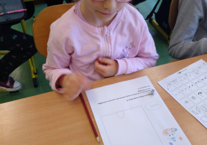 Dziewczynka siedzi w ławce i wykonuje zadanie na karcie pracy