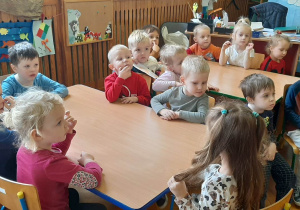 Dzieci siedzą przy stolikach, słuchają wypowiedzi pracowników Straży Miejskiej