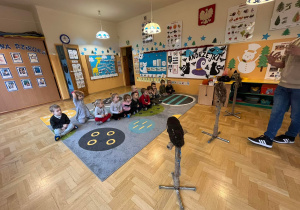 Dzieci siedzą na dywanie i słuchają ciekawostek o sowach