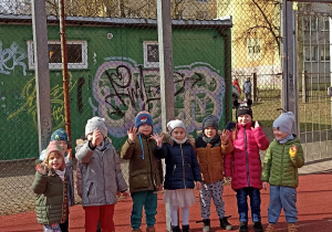 dzieci stoją pod koszem na boisku i machają