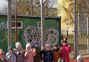 dzieci stoją pod koszem na boisku i machają