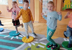 dzieci stoją na jednej nodze na kolorowym krążku
