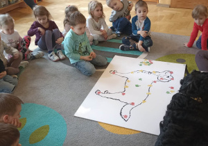 dzieci siedzą w kole. Na dywanie leży duża plansza psa