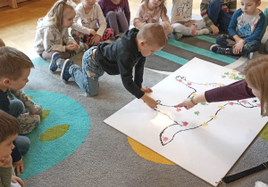 dzieci siedzą w kole. Na dywanie leży duża plansza psa