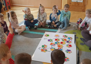 dzieci siedzą w kole. Na dywanie leży duża plansza psa