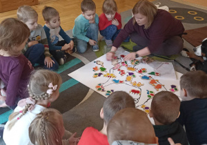 dzieci siedzą w kole. Na dywanie leży duża plansza psa