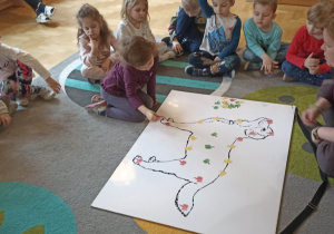 dzieci siedzą w kole. Na dywanie leży duża plansza psa