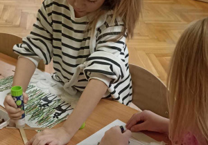 dzieci siedzą przy stole i rysują choinki