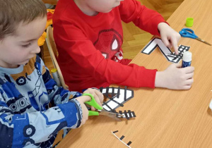 dzieci wyklejają literę z czarnymi paskami