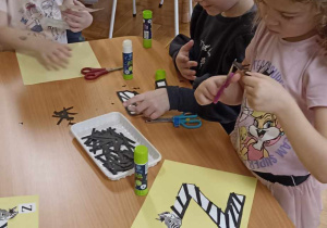 dzieci wyklejają literę z czarnymi paskami
