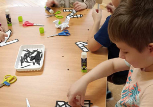 dzieci wyklejają literę z czarnymi paskami