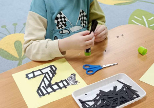 dzieci wyklejają literę z czarnymi paskami