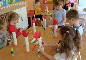 dzieci doklejają elementy z papieru kolorowego do rolki