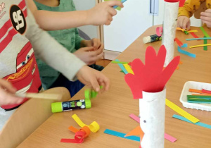 dzieci doklejają elementy z papieru kolorowego do rolki