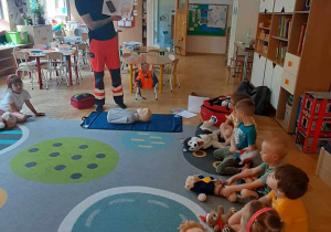 Dzieci siędz w kole i słuchają bajki czytanej przez ratownika
