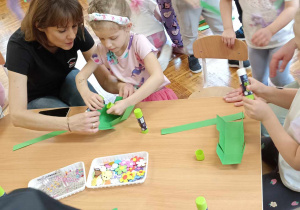 rodzice i dzieci przy stole ozdabiają koszyczek i jajko