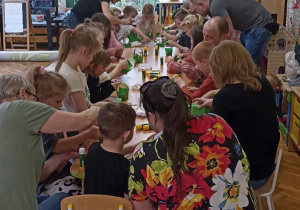 rodzice i dzieci przy stole ozdabiają koszyczek i jajko