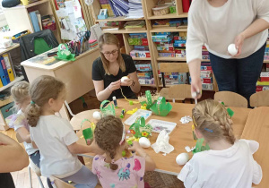 rodzice i dzieci przy stole ozdabiają koszyczek i jajko