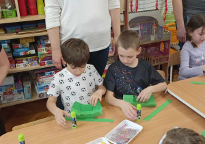 rodzice i dzieci przy stole ozdabiają koszyczek i jajko