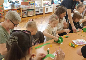 rodzice i dzieci przy stole ozdabiają koszyczek i jajko
