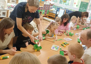 rodzice i dzieci przy stole ozdabiają koszyczek i jajko