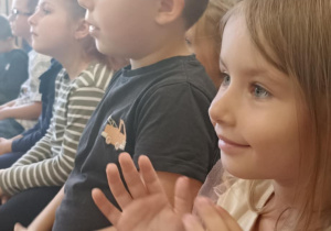 dzieci siedzą na ławce i klaszczą