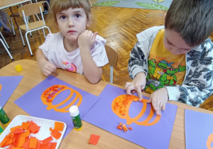 dzieci wyklejają bibułą sylwetę dyni