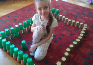Dziewczynka pozuje obok budowli z kubeczków