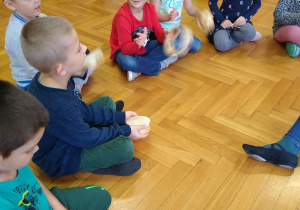 Dzieci siedzą na podłodze, trzymają instrumenty perkusyjne
