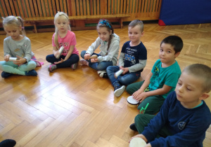 Dzieci siedzą na podłodze, trzymają instrumenty perkusyjne