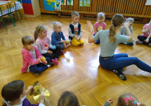 Dzieci siedzą na podłodze, trzymają instrumenty perkusyjne