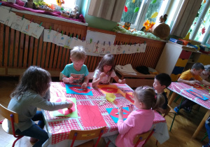 Dzieci wycinają usta z kartki, czerwonego papieru, naklejają fasolę