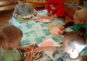 dzieci siedzą przy stole i naklejają kolorowe elementy z papieru